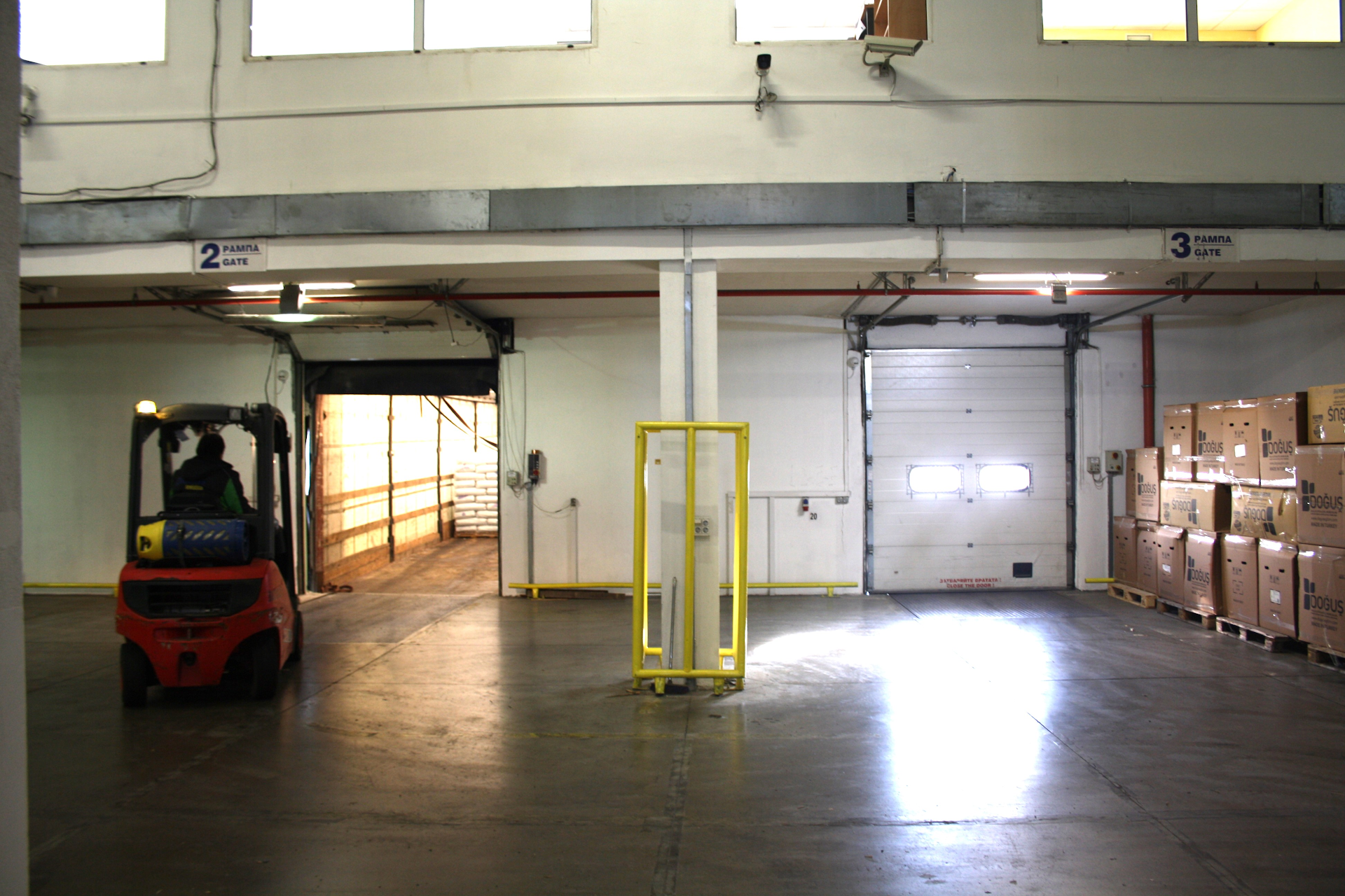 Busy warehouse interior with forklift operation, stacked boxes, and open loading dock gates