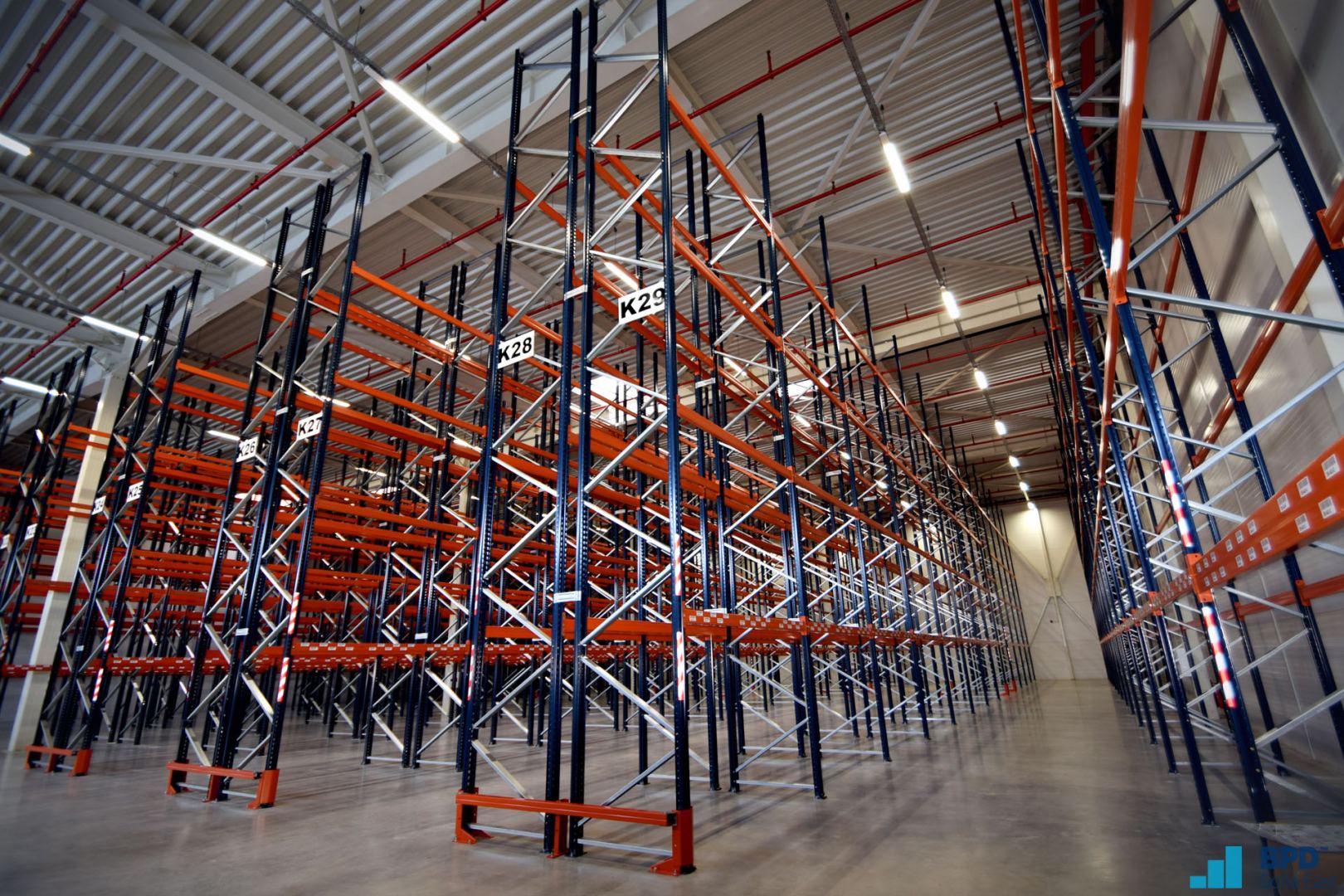 Rows of empty industrial metal shelving units inside a vast, well-lit warehouse